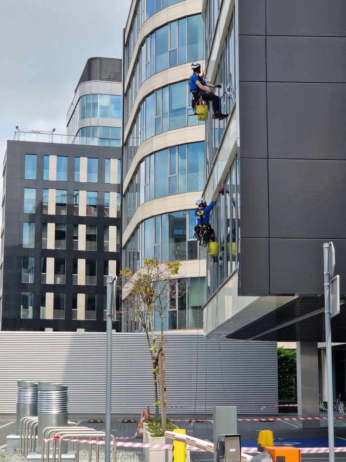 Two workers are cleaning windows on a tall office building in an urban setting.